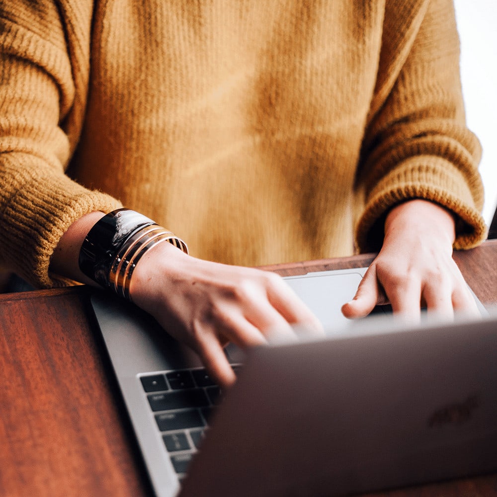 Woman in orange sweater typing on laptop