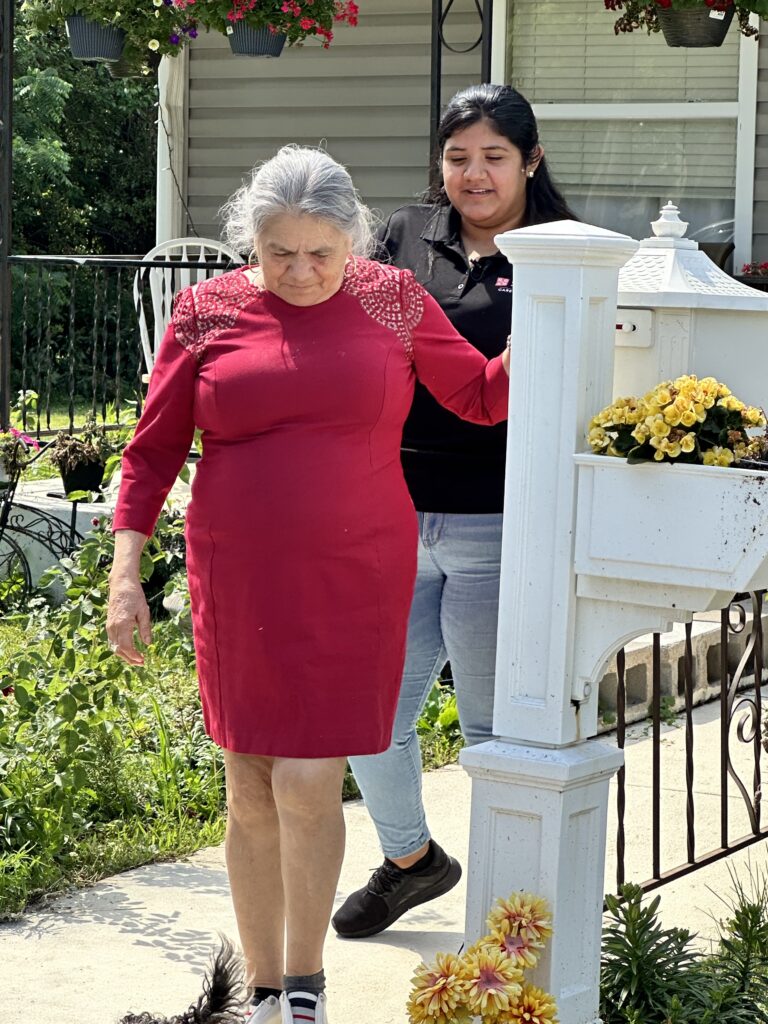older woman walking to mailbox with young woman caregiver walking behind her